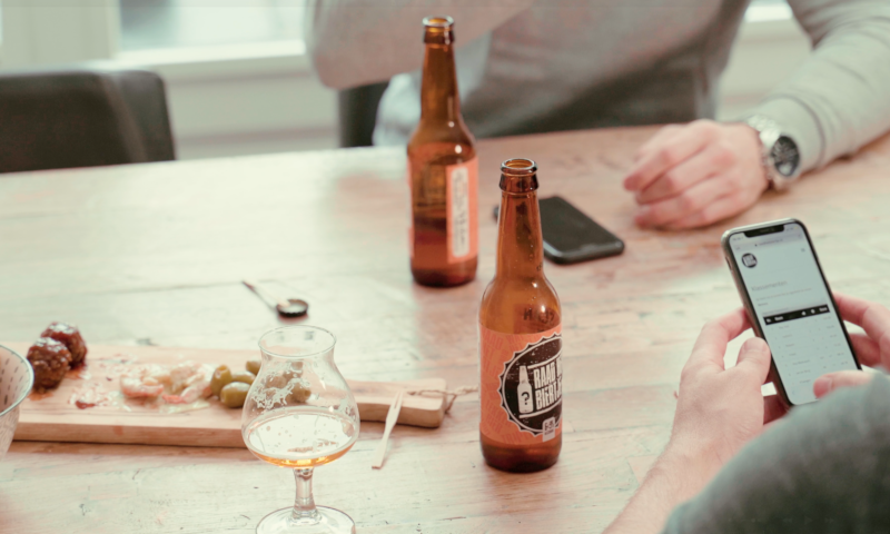 Man houdt telefoon vast en er staan biertjes op tafel van raadhetbiertje.nl
